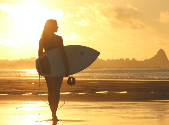 Kobieta z deską surfingową na tle zachodu słońca