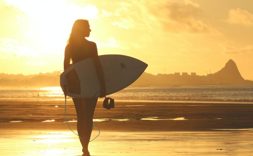 Kobieta z deską surfingową na tle zachodu słońca